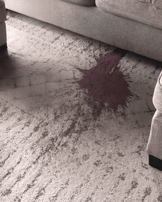 Large red wine stain on beige carpet in living room